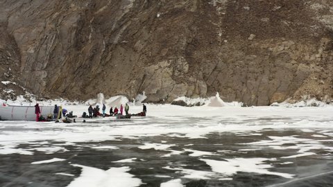 Drone flight close to the ice for tourists with a tent and rocky shore. Tent on frozen Lake Baikal and tourists preparing for the night