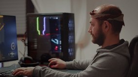 Portrait of young pro gamer man sitting at powerful personal computer looking into camera. Concentrated cyber playing first-person space shooter online video game performing during gaming tournament