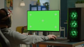 Pro gamer streaming video games with green screen mock-up display in gaming home studio. Player using RGB professional computer with chroma key isolated desktop playing shooter games wearing headset
