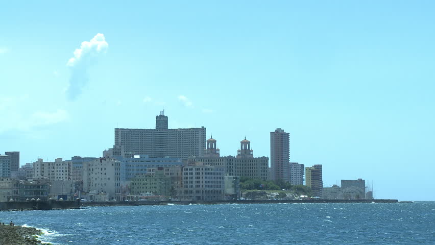 View from the Malecón in Cuba, Havana, showing the Caribbean sea and several large buildings in the distance. The famous Hotel Nacional de Cuba is visible in the distance.