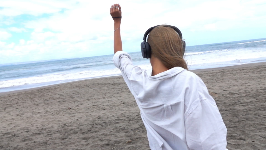Happy, pretty woman listen to music, dance on the beach, slow motion