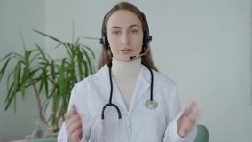 Woman doctor in white medical uniform with stethoscope talk video conference call with patient, looking at camera.