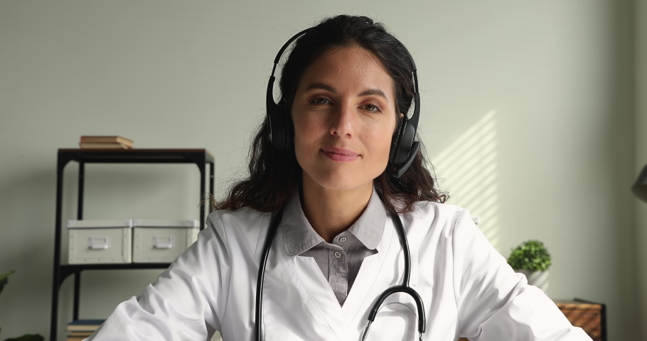 Concentrated skilled young female physician doctor wearing headphones with microphone, giving online virtual consultation to patient or taking part in video conference, medical service concept. Royalty-Free Stock Footage #1070084782
