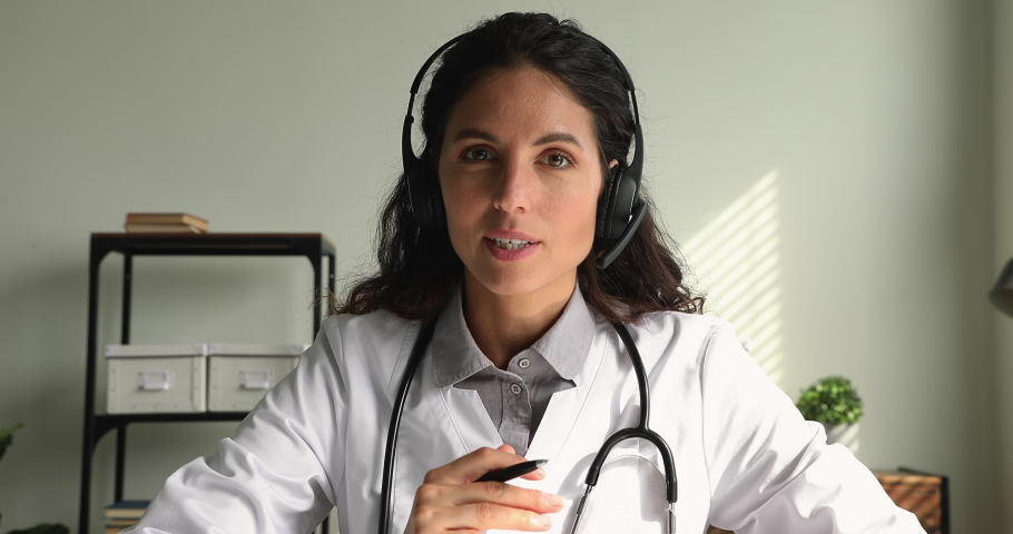 Concentrated skilled young female physician doctor wearing headphones with microphone, giving online virtual consultation to patient or taking part in video conference, medical service concept. | Shutterstock HD Video #1070084782