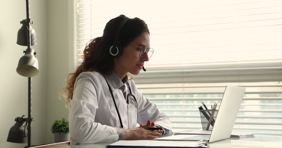 Side view professional 35s female doctor physician wearing headset, giving online web camera video call consultation online to patient, using computer application, modern tech telemedicine concept. | Shutterstock HD Video #1070084785