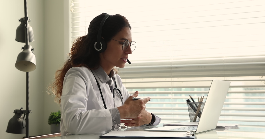 Side view professional 35s female doctor physician wearing headset, giving online web camera video call consultation online to patient, using computer application, modern tech telemedicine concept. Royalty-Free Stock Footage #1070084785