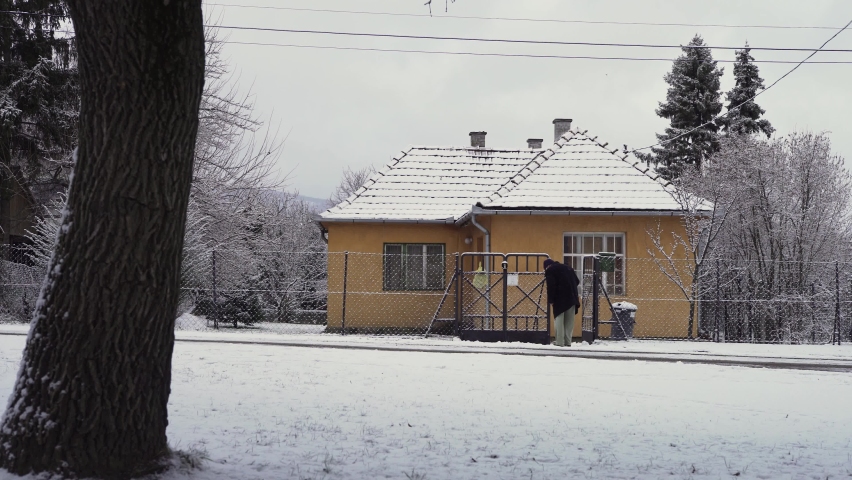 Elderly man shovels snow in front of his house.