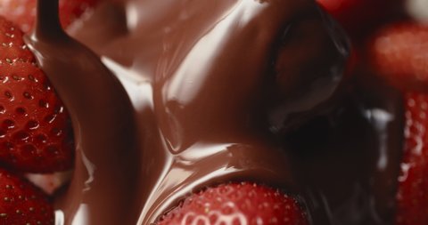 Close-up macro fresh strawberries covering with melted liquid chocolate. Molten chocolate or brown caramel stream pouring on juicy red berries. Confectionery, tasty dessert. Cooking handmade sweets