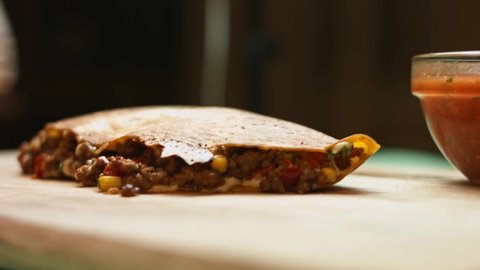 Cutting a freshly fried hot beef quesadilla on a wooden cutting board. Process of making mexican quesadillas. Side view