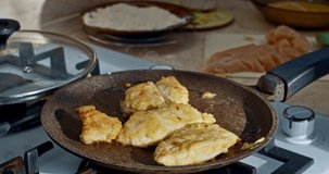 Female hand in home kitchen putting breaded chicken in a frying pan