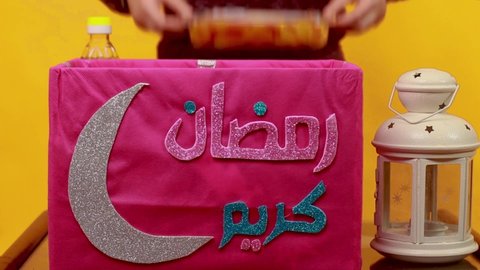 Young Muslim girl preparing Ramadan food box for charity - Ramadan Kareem , English Translation : Ramadan is the month of giving