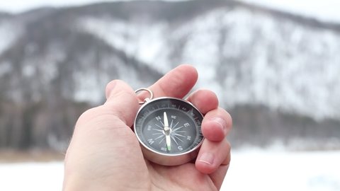 A tourist uses a compass. Compass on the background of snowy mountains. Hiking equipment
