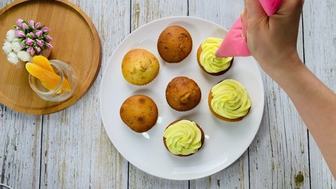 Apply cream to cupcakes. Squeeze yellow cream from pastry bag. Beautiful desserts for the holiday.