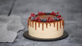 Female hands cutting delicious caramel cake with frozen summer berries.