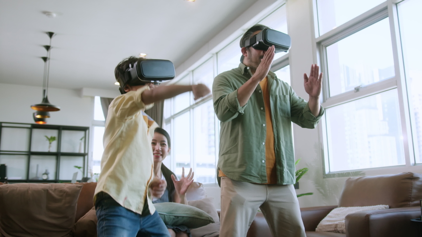 asian family Dad and son wear VR or virtual reality glasses,headsets standing and playing a video game at living room in  front of TV at home in quarantine period technology and innovation concept Royalty-Free Stock Footage #1070108140