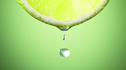 Super Slow Motion Macro Shot of Lime Juice Drop Falling from Lime Slice on Green Background at 1000fps.