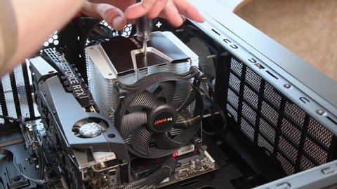 Male hands with screwdriver unassemble CPU cooler from motherboard with NVidia GeForce RTX graphics card installed inside gaming PC tower. Processor cooler fan assembling. Odessa, Ukraine, 04 04 2021