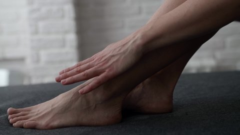 female feet on bed or couch, woman is stroking her skin by fingers, closeup view, tenderness and foot fetish concept