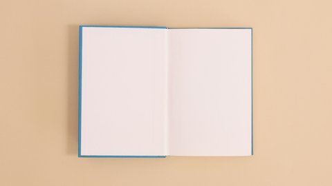 6k Blue hardcover vintage book appear and open with copy space on beige background. Stop motion flat lay
