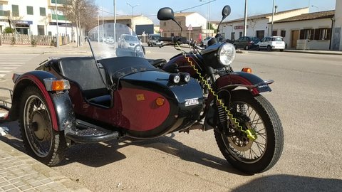 Campos, Spain; march 26 2021: Dark colored motorcycle with sidecar parked on a sunny street in Mallorca with vehicle traffic in the background