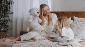 Little girl caucasian daughter preschool child kid sitting with mother beloved mom in bed in bedroom kisses teddy bear playing with toy, single parent woman mommy have fun with baby in morning at home - Powered by Shutterstock - Get 15% off with code: PIKWIZARD15