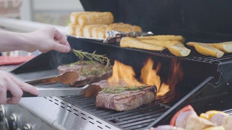 Grilling New York steak with a slice of butter and rosemary on an outdoor gas grill.