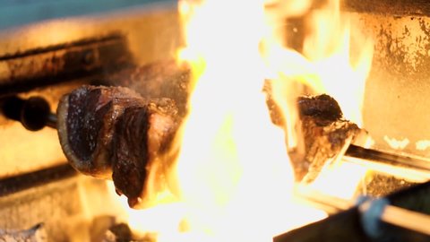 Huge flames cooking raw piece of beef rump cap on open fire barbeque