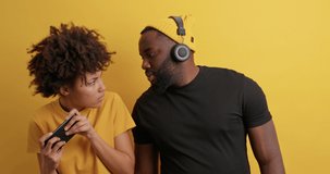 Addicted Afro American woman plays video games holds smartphone ignores boyfriend doesnt show results dressed casually. Dark skinned guy listens music via wireless headphones needs live communication