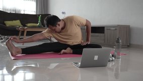 asian Fit Young Man Exercise on Mat at home. stretching and workout by himself looking at laptop video