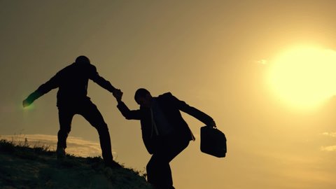 Two businessmen climb to top of mountain. Helping hand in business. Teamwork in business. Businessmen help to overcome difficulties. Helping hand in teamwork. Business partnership business success