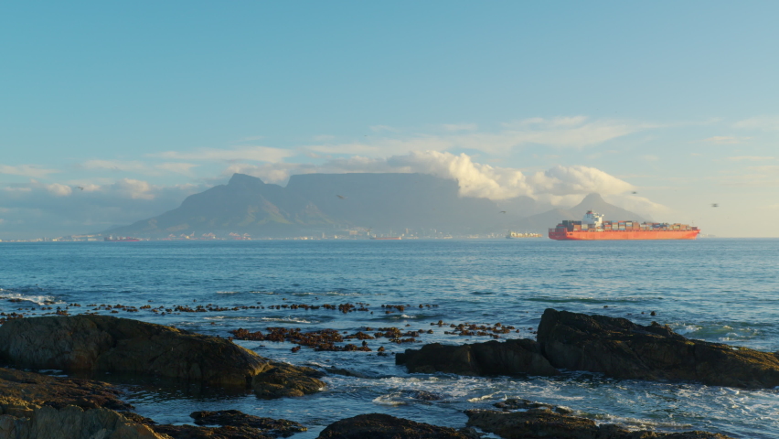 Capetown. Beautiful clear day looking to table mountain and mother city with ocean waves crashing over rocky shore line.