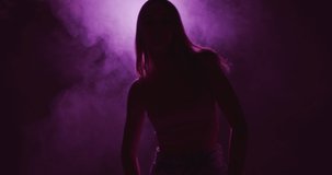 Dancing young girl in violet neon light and haze. 4k video of female silhouette and smoke at night. Modern dance