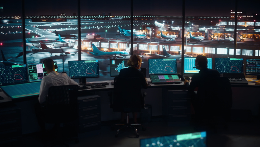 Diverse Air Traffic Control Team Working in a Modern Airport Tower at Night. Office Room is Full of Desktop Computer Displays with Navigation Screens, Airplane Flight Radar Data for Controllers.