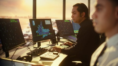 Portrait of Male Air Traffic Controller with Headset Talk on a Call in Airport Tower. Office Room is Full of Desktop Computer Displays with Navigation Screens, Airplane Flight Radar Data.
