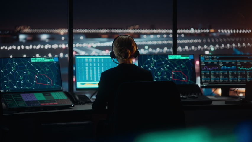 Female Air Traffic Controller with Headset Talk on a Call in Airport Tower at Night. Office Room is Full of Desktop Computer Displays with Navigation Screens, Airplane Flight Radar Data for the Team. | Shutterstock HD Video #1070147608