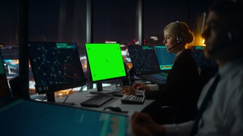 Female Air Traffic Controller with Headset Works on Computer with Green Screen Mock Up in Airport Tower. Office Room with Displays with Navigation Screens, Airplane Flight Radar Data for the Team.