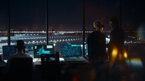 Female and Male Air Traffic Controllers with Headsets Talk in Airport Tower at Night. Office Room Full of Desktop Computer Displays with Navigation Screens, Airplane Flight Radar Data for Controllers.