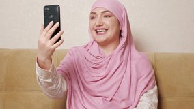 Beautiful muslim woman in hijab talking by video call while sitting on the couch.
