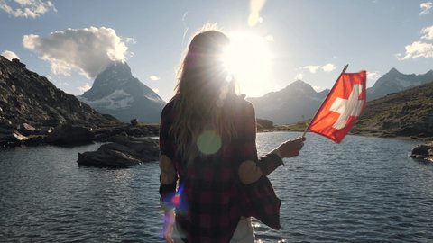 Female holding Swiss flag against mountain landscape with the Matterhorn peak in the background 