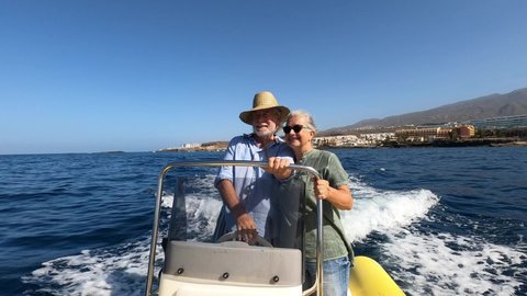 Beautiful and cute couple of seniors or old people in the middle of the sea driving and discovering new places with small boat. Mature woman holding a phone and taking a selfie with hew husband
