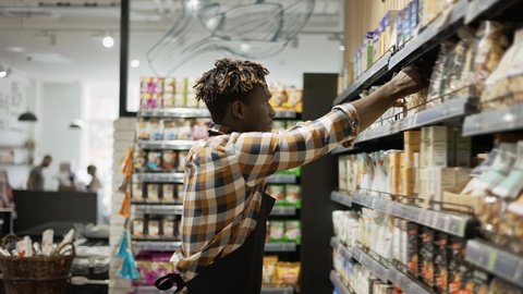 African american worker in apron arranging shelves with products at grocery shop