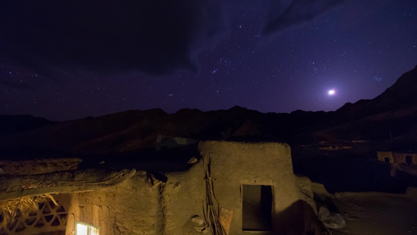 Old Village House at Night and Moon and Stars and Orion Nebula sets Over the Mountains in Background Landscape