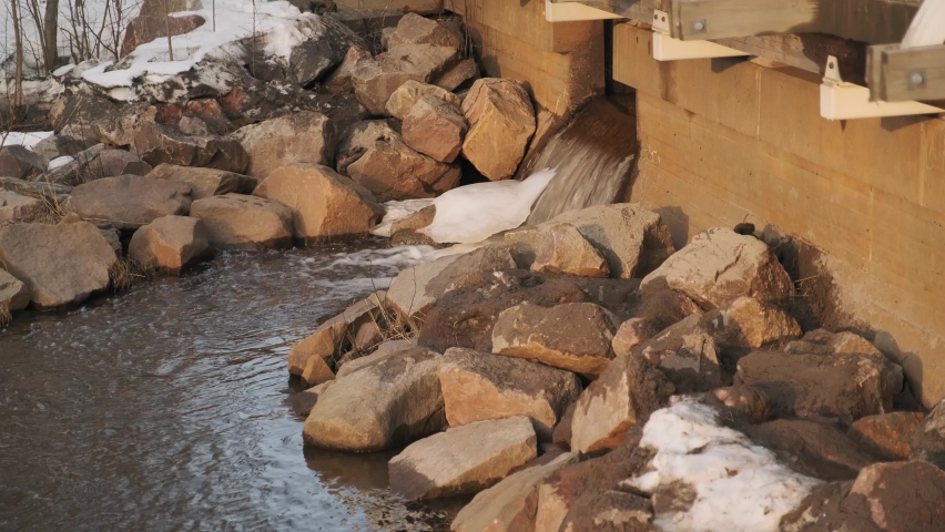 Cold Stream of Water Flowing under a Bridge during a Sunset in Early Spring