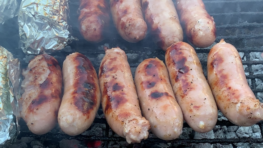 Barbecue braai sizzling hot pork sausages grilled over hot coals and mielies wrapped in foil Royalty-Free Stock Footage #1070153467