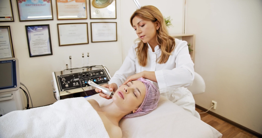 Woman in a spa salon on cosmetic procedures for facial care. Cosmetologist making a woman a therapeutic procedure on a face. Beautician makes medical procedures using a professional  equipment.
 | Shutterstock HD Video #1070153884