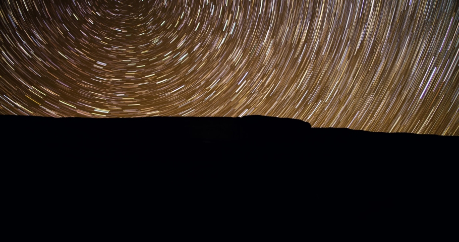 Star trails time lapse of night sky over rocky beach landscape