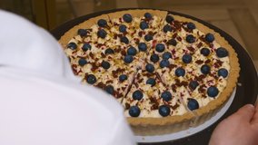 Sliced berry pie is laid out on a round dark brown tray. The waiter slowly carries a tray of blueberry pie. The video was shot in close-up from behind.