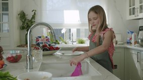 Happy two girls sisters washing dishes and playing with foam in kitchen. Children having fun with pink gloves. Slow motion 4K UHD video 50 fps