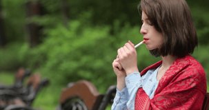 Beautiful woman smokes cigarette in park. 4K video.
