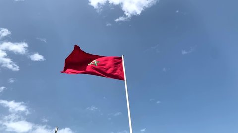 Slow-motion 4K footage of the Moroccan red flag waving around outdoors with a blue sky in the background